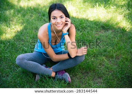 Smiling beautiful fitness woman sitting on the green grass outdoors and looking at camera