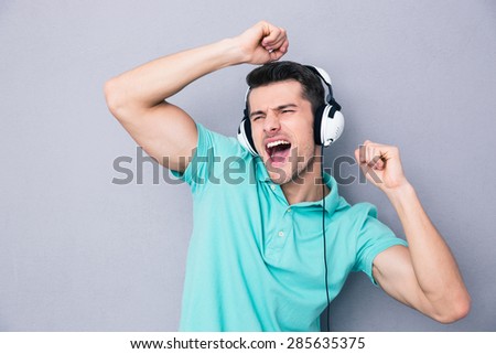 Handsome young man singing in headphones over gray background