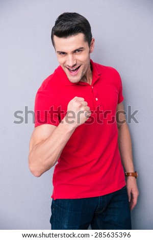 Happy handsome man showing fist over gray background and looking at camera