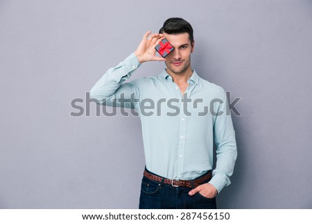 Handsome man covering his eye with gift box over gray background and looking at camera