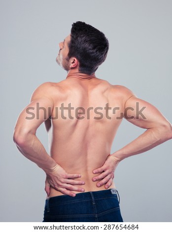 Muscular man having pain in back over gray background