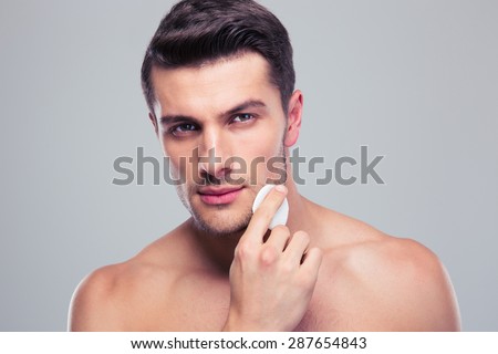 Man cleaning face skin with batting cotton pads over gray background