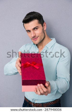 Happy man giving gift box on camera over gray background