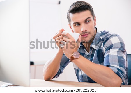 Handsome businessman sitting at the table and drinking coffee in office. Looking away