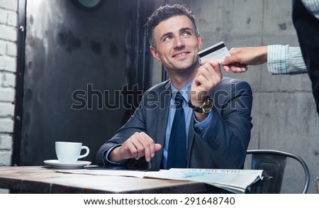 Happy businessman passing his credit card to waiter in cafe
