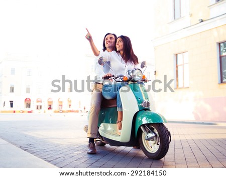 Happy young couple on scooter together while woman pointing finger away in the town