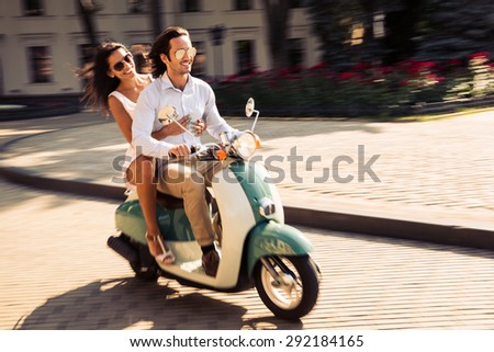 Cheerful young couple riding a scooter in town with fun