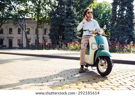 Confident young man on scooter talking on the phone outdoors