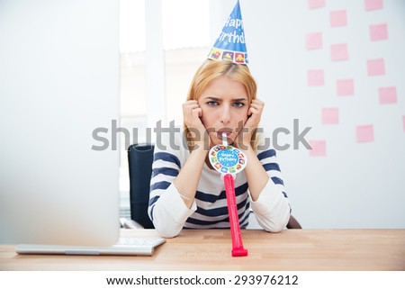 Young girl sitting at the table with party hat in office and blows whistle