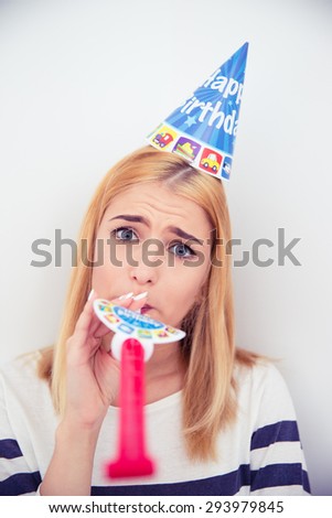 Young girl with party hat and blows whistle over gray background. Looking at camera