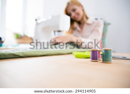 Female designer sitting at the table and working on sewing machine. Focus on equipment