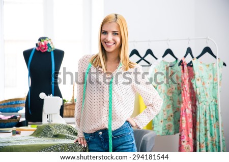 Happy female tailor standing in workshop and looking at camera