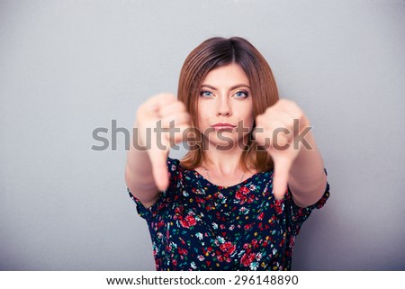 Portrait of a woman showing thumbs down over gray background. Looking at camera