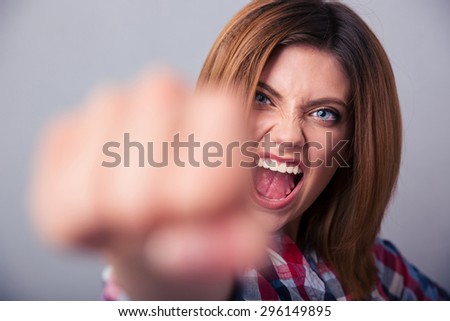 Angry woman hitting with fist on camera and shouting over gray background