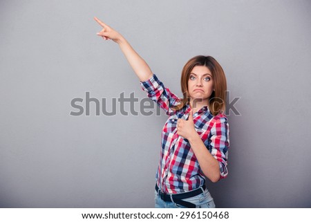 Beautiful young woman showing thumb up and pointing finger up over gray background