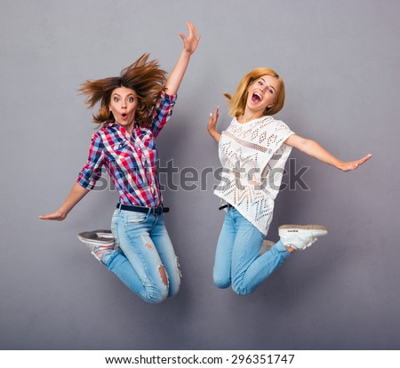 Two cheerful girls jumping over gray background