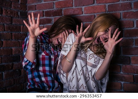 Two frightened woman standing with brick wall on background