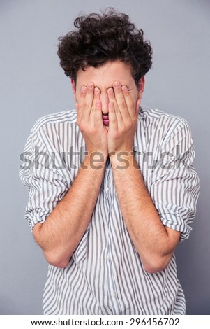 Young man covering his face with palms over gray background