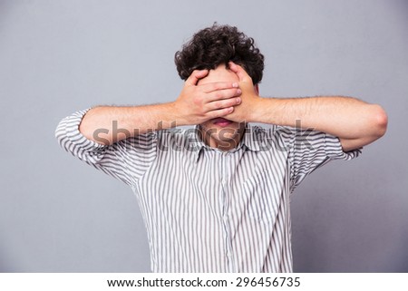 Man covering his eyes with hands over gray background