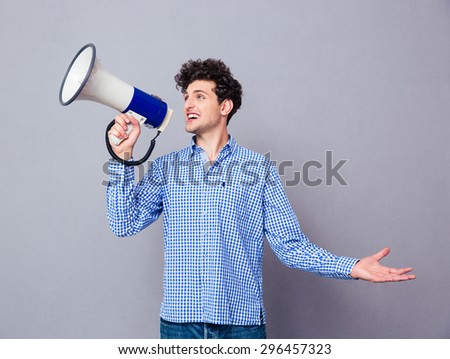 Young casual man screaming on megaphone over gray background