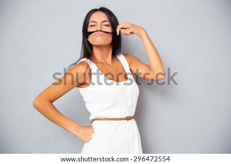Young woman making mustache with hair over gray background