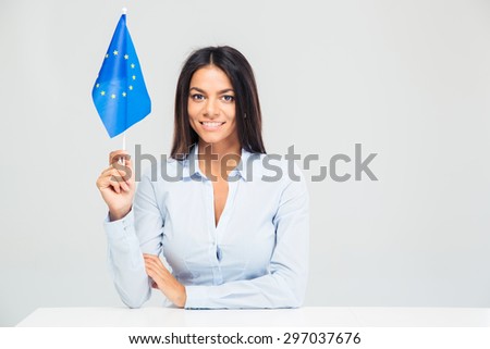 Happy businesswoman sitting at the table with european flag isolated on a white background. Looking at camera