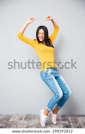 Portrait of a happy young woman dancing on gray background
