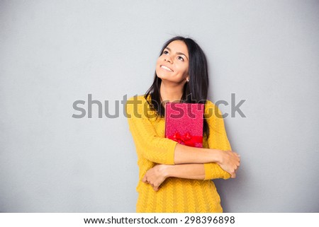 Happy thoughtful woman holding gift box and looking up over gray background