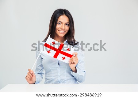 Smiling young woman sitting at the table with georgian flag isolated on a white background. Looking at camera