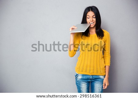 Casual woman biting tablet computer over gray background