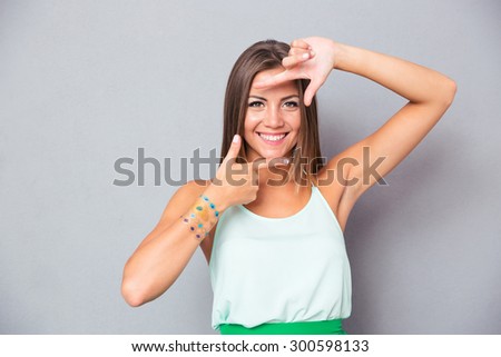 Smiling beautiful girl making frame gesture with fingers over gray background