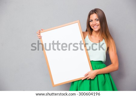 Happy girl holding blank board over gray background and looking at camera