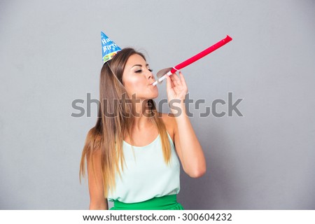 Young girl in party hat blowing in whistle over gray background