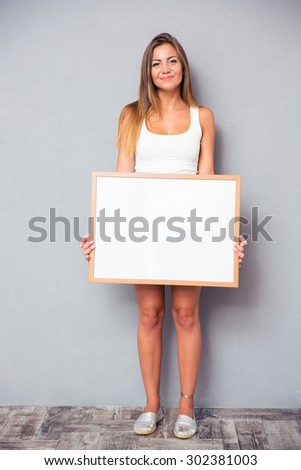 Pretty young girl holding blank board on gray background. Looking at camera