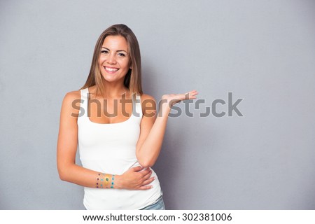 Cheerful pretty girl holding copyspace on the palm over gray background