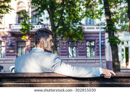 Back view portrait of a handsome businessman sitting on the bench outdoors
