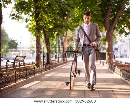 Pensive young businessman walking with bicycle on the street in town