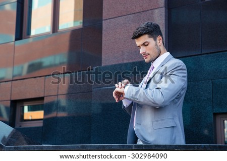 Businessman looking on wrist watch outdoors near office building