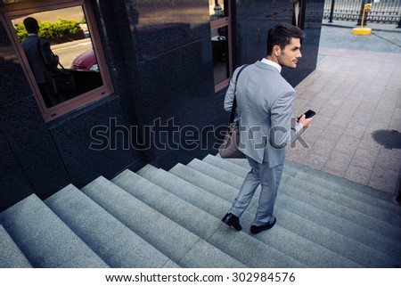 Businessman with smartphone walking on the stairs outdoors and looking  away