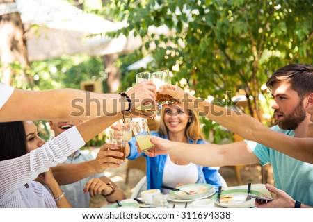 Group of a smiling friends making toast around table at dinner party in outdoor restaurant