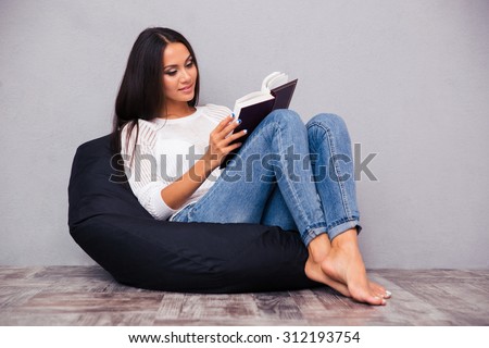 Beautiful woman sitting on the bag chair and reading book on gray background