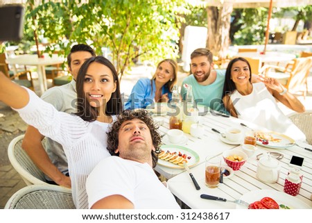 Portrait of a happy friends making selfie photo in outdoor restaurant