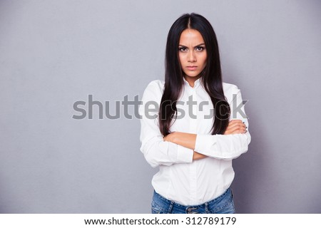 Portrait of angry woman standing with arms folded on gray background