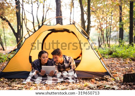 Portrait of a smiling couple lying in tent and using tablet computer in forest