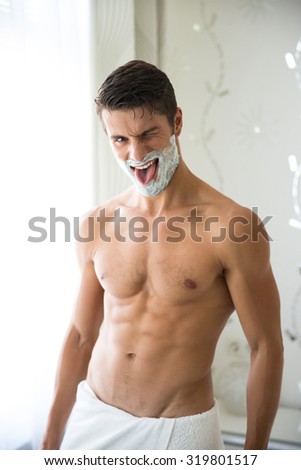 Portrait of a funny naked man with foam on face standing in bathroom