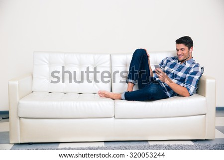 Portrait of a casual man with headphones using smartphone on the sofa