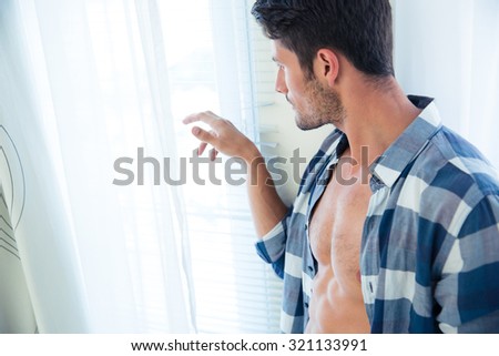 Portrait of a handsome man looking in window at home