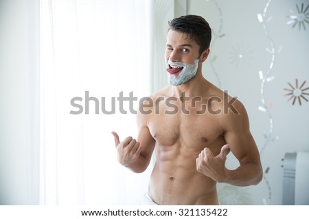 Portrait of a funny man with foam on face showing thumbs up in bathroom