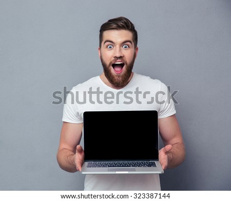 Portrait of a cheerful man showing blank laptop computer screen over gray background