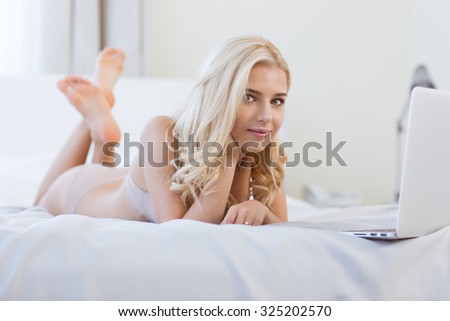 Portrait of a happy blonde girl lying on the bed with laptop computer